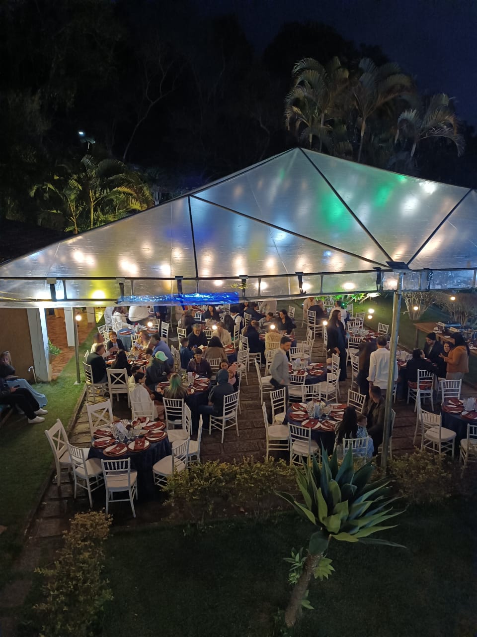 Confraternização noturna sob tenda iluminada com mesas decoradas